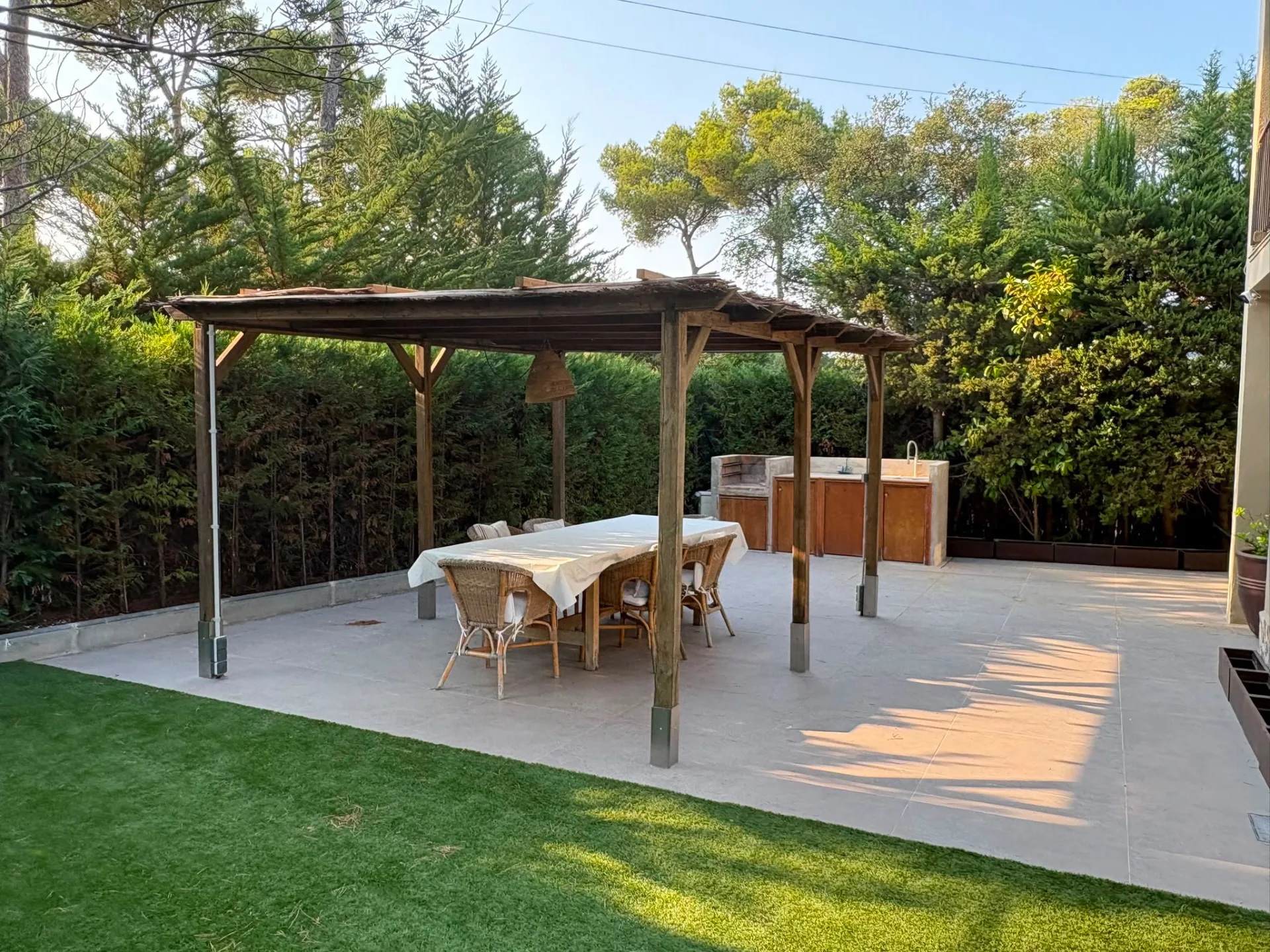 Terrace with a timber pergola, long dining table and outdoor kitchen beside the lawn — Mediterranean Home on the Costa Brava