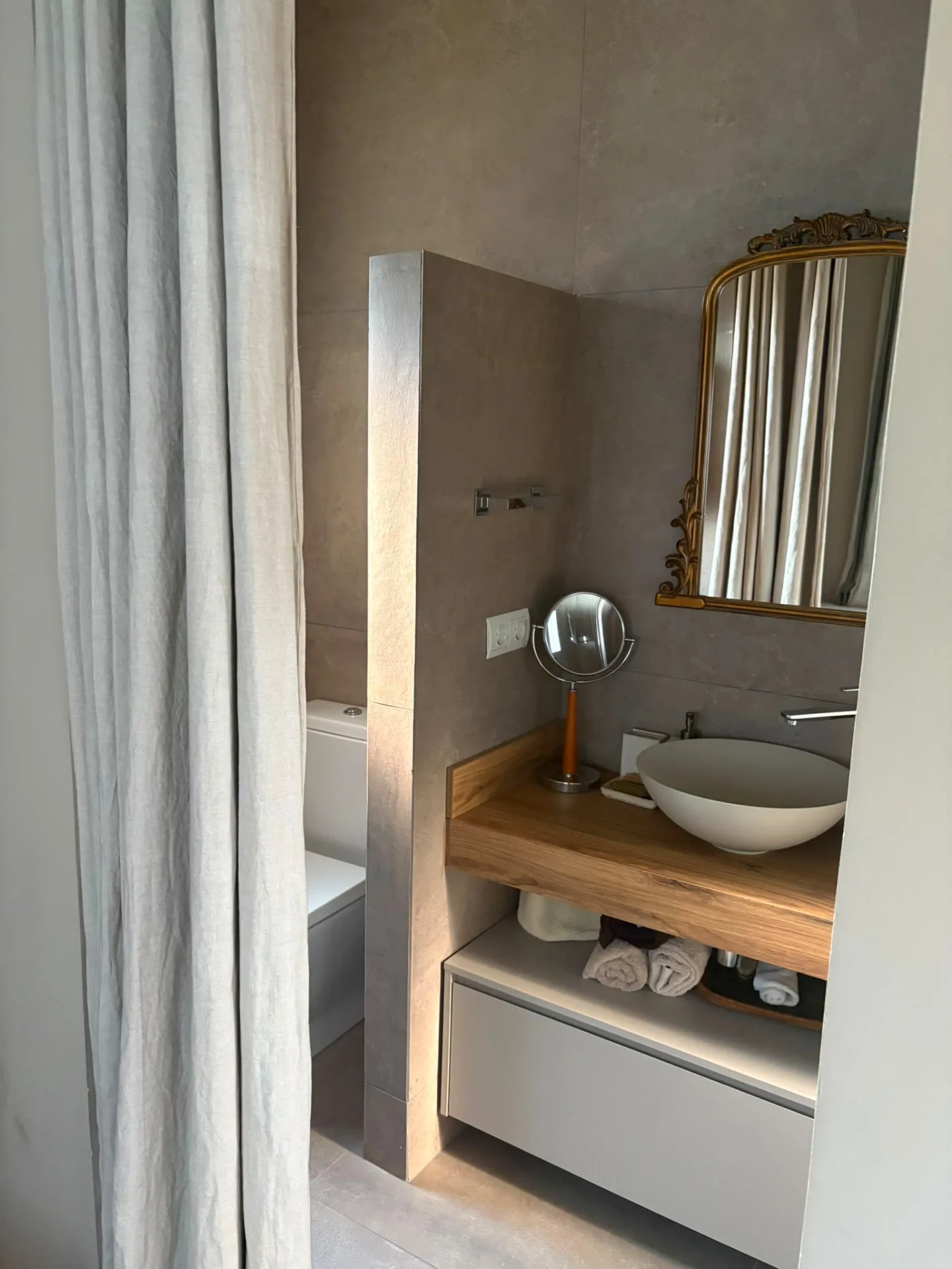Bathroom with a solid timber vanity, a round basin and a gilded classical mirror against microcement surfaces — Mediterranean Home on the Costa Brava