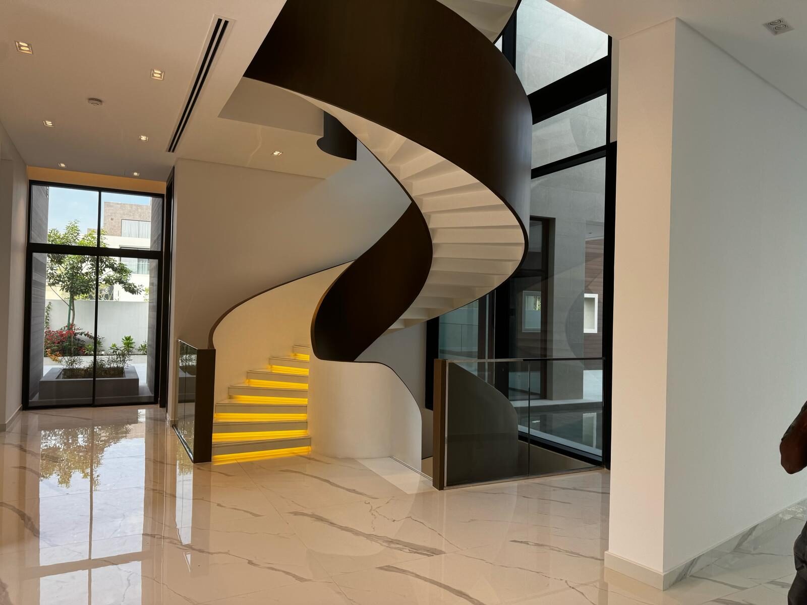 Spiral staircase with dark cladding and lit white treads, marble floor and glazing onto the patio — Contemporary International Villa