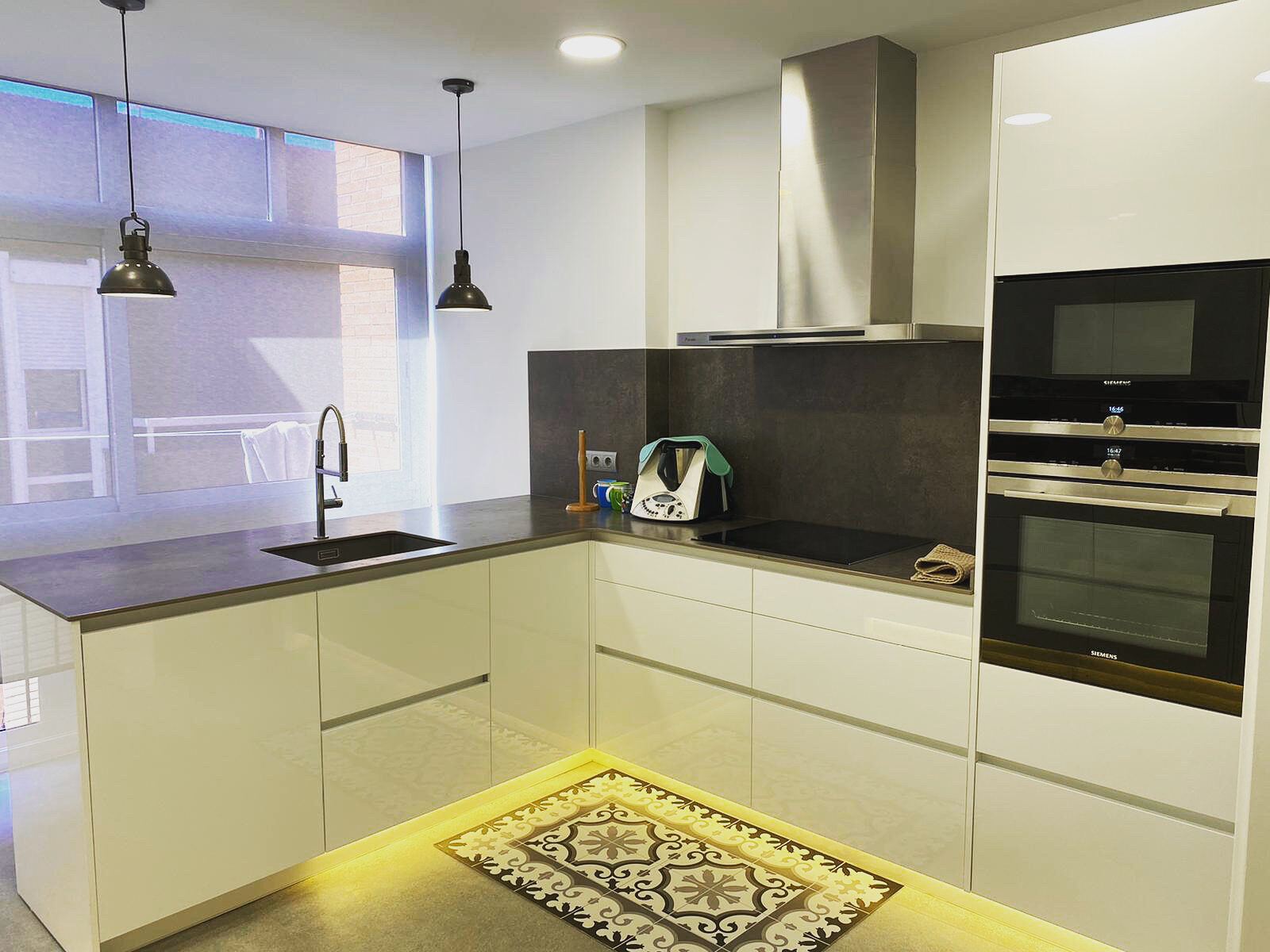 Kitchen with white cabinetry, dark worktops, a large window and a patterned rug — Family Home in Barcelona’s Upper Districts