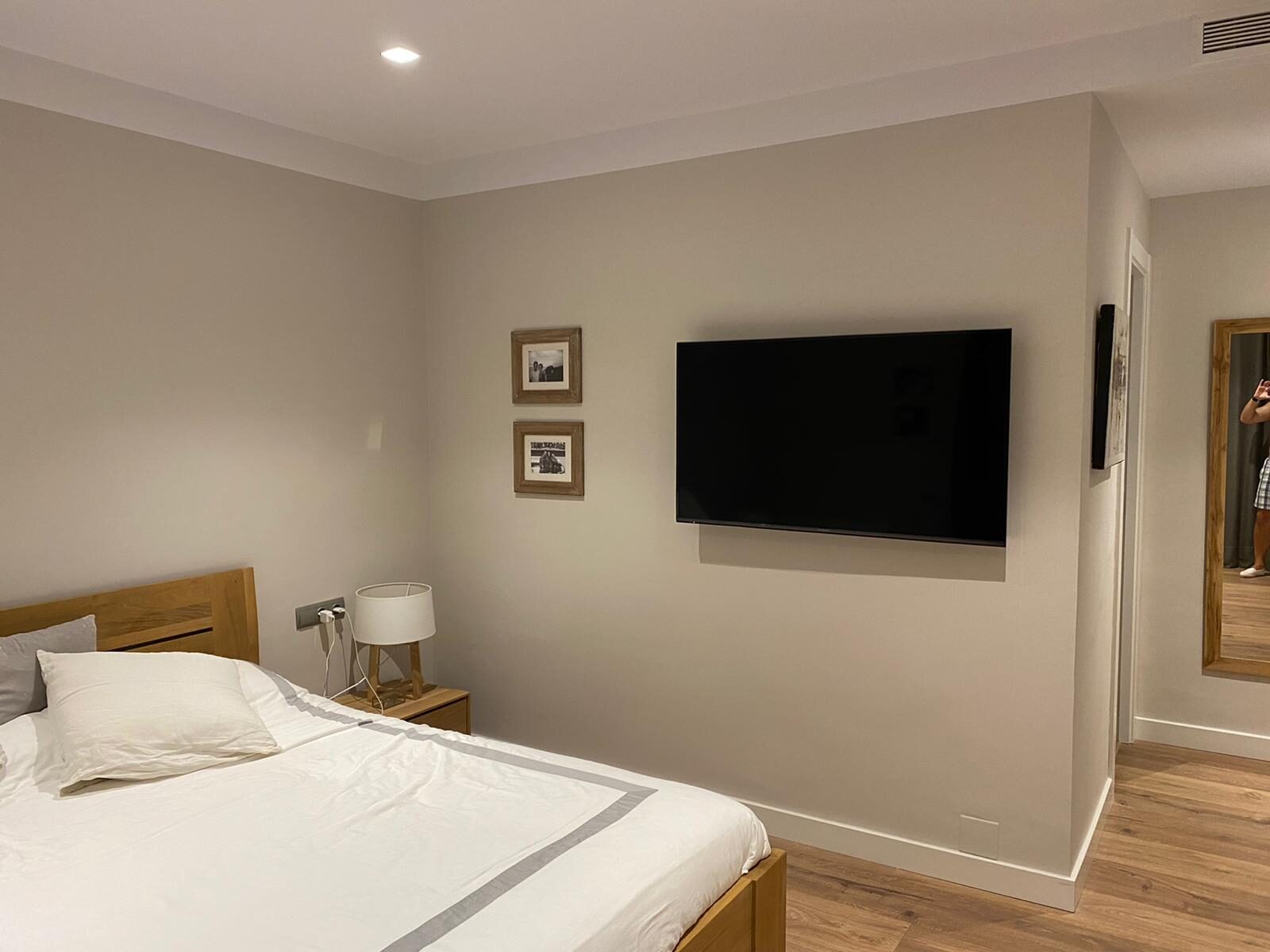 Main bedroom with a wooden bed frame, neutral walls and a wall-mounted television — Family Home in Barcelona’s Upper Districts